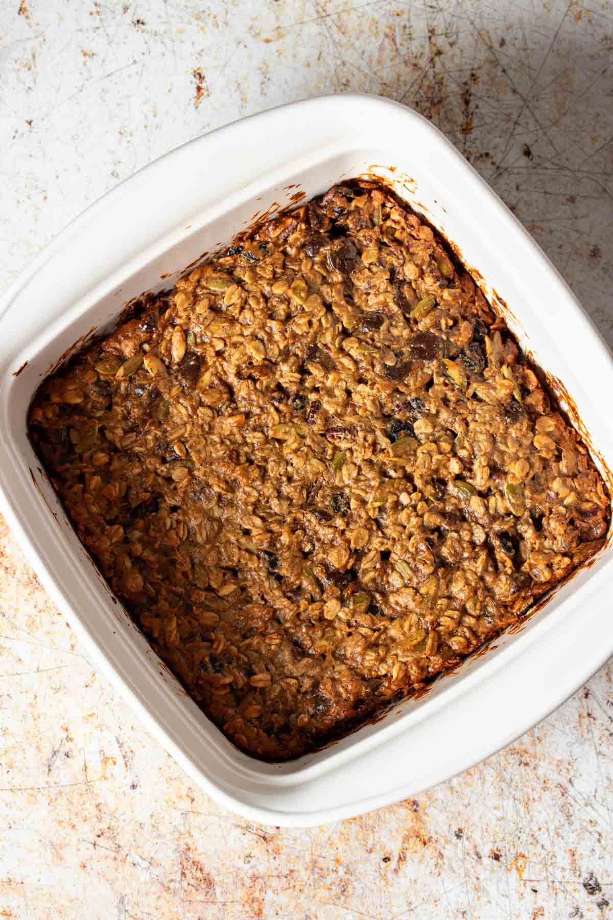 Top view of a white square baking dish with baked breakfast bar dough inside of it sitting on a lighter surface.