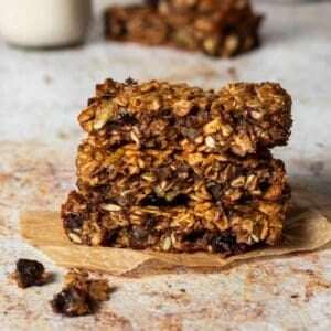 Three oat breakfast bars stacked on top of each other sitting on a piece of parchment paper.