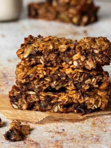 Three oat breakfast bars stacked on top of each other sitting on a piece of parchment paper.