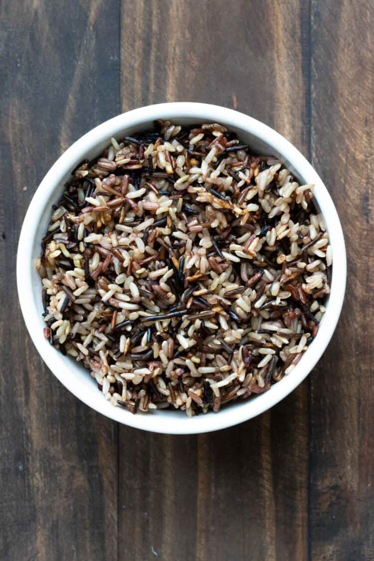 A white bowl with cooked wild rice in it on a wooden surface.