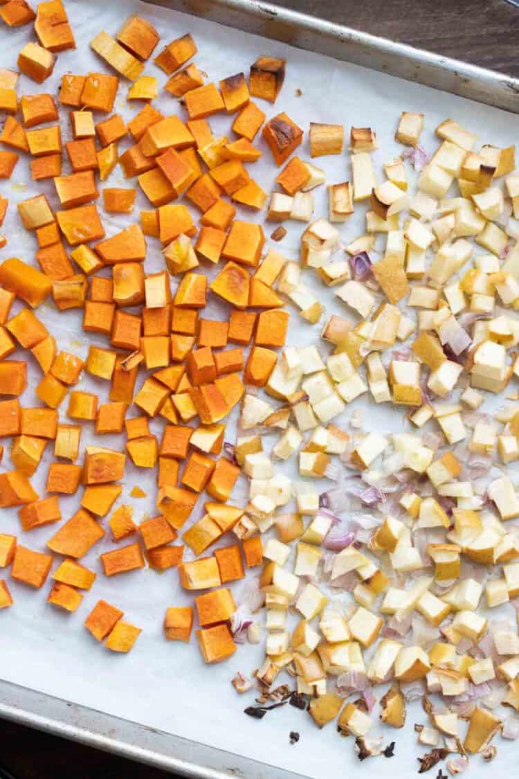 Top view of a baking sheet with parchment and half chopped butternut squash and have chopped apples.