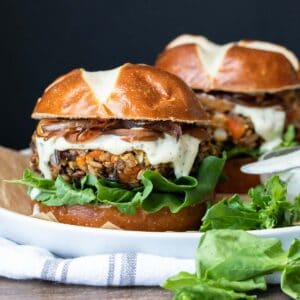 Two burgers with pretzel buns and rice based burgers topped with white sauce and lettuce.
