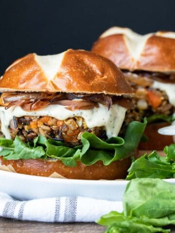 Two burgers with pretzel buns and rice based burgers topped with white sauce and lettuce.