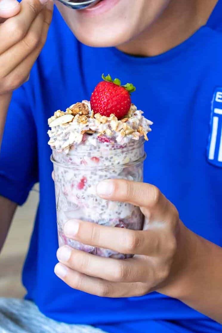 Boy in blue shirt smiling and eating from a jar of overnight oats