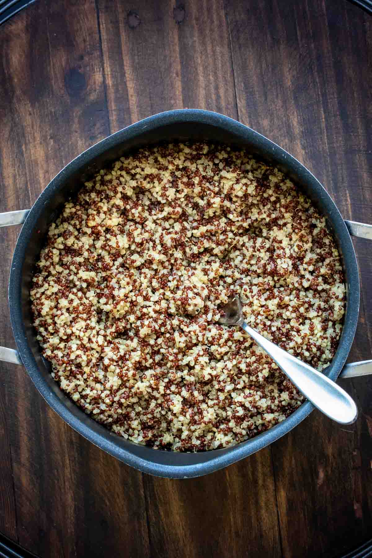 Top view of cooked quinoa in a black pot with a spoon in it.