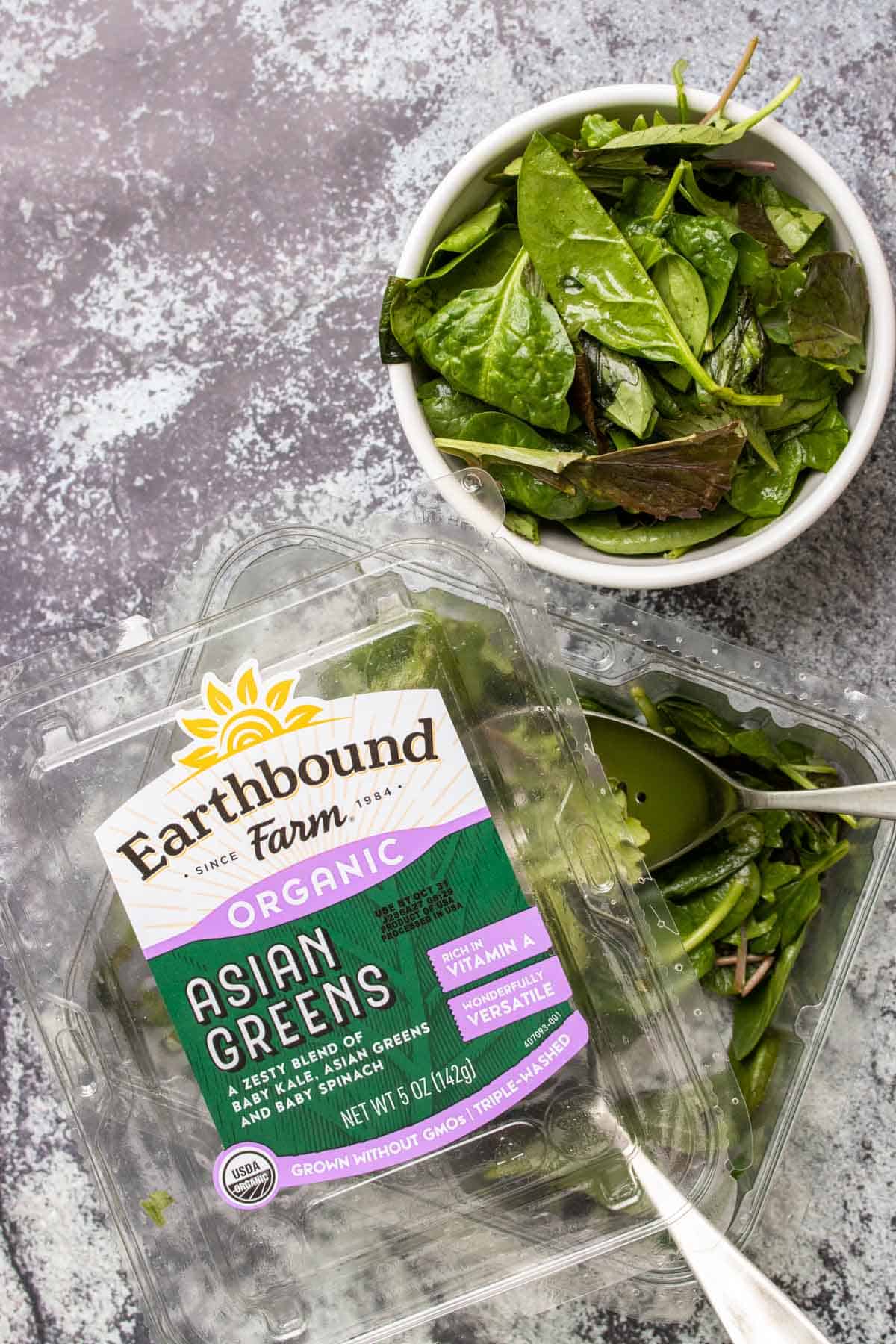 Salad being served out of its plastic container next to bowl of salad.