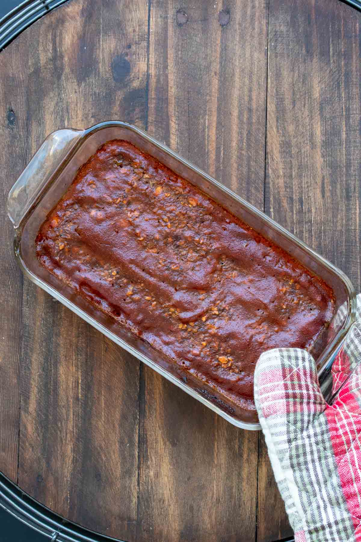 Oven mitt holding a glass loaf pan with baked lentil meatloaf in it.