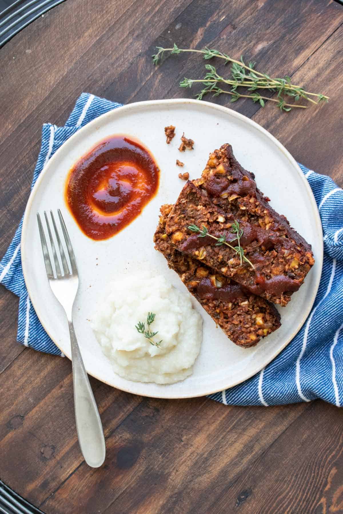 A white plate with slices of lentil meatloaf and mashed cauliflower with a scoop of sauce.