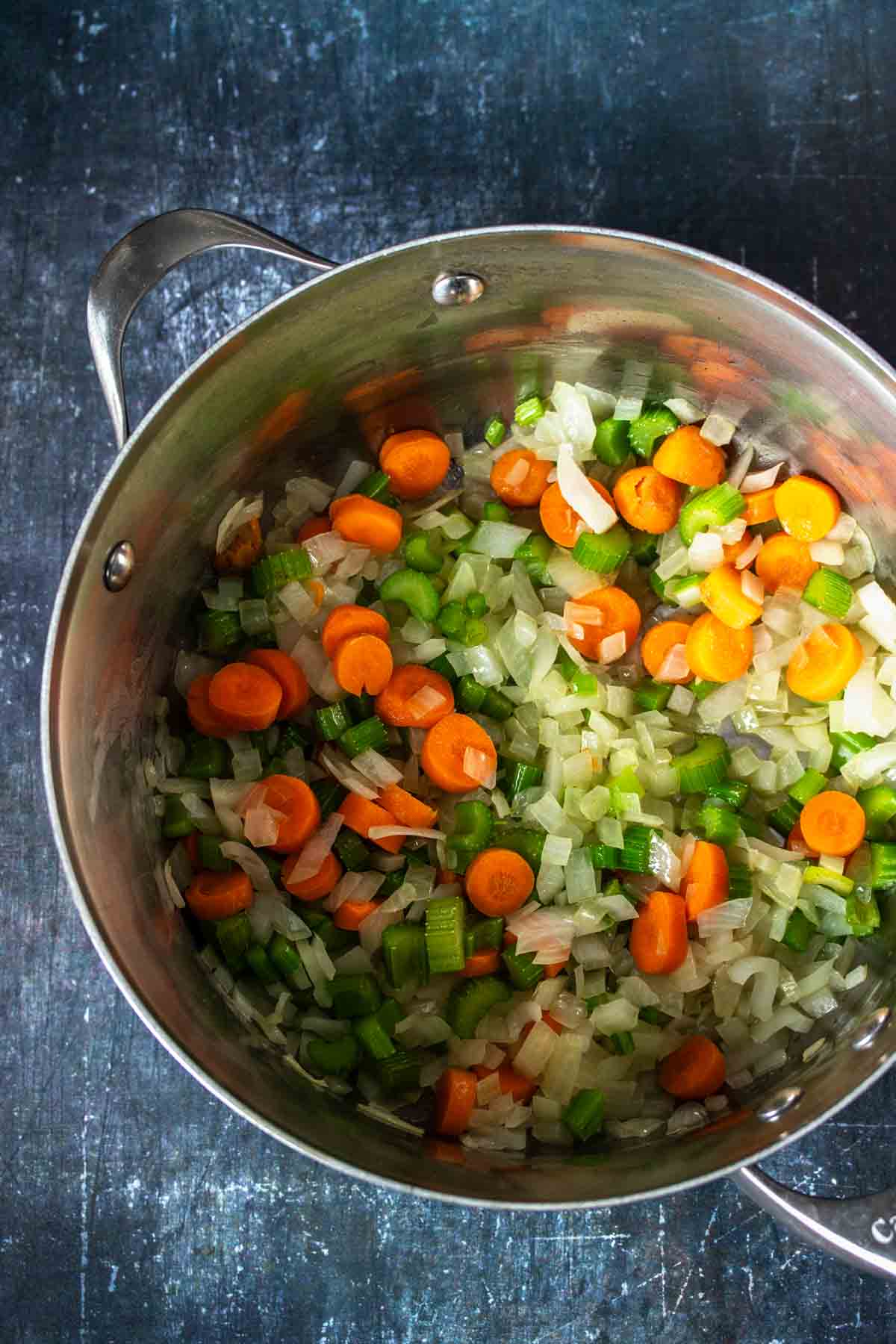 Top view of a metal soup pot with onion, carrots and celery inside.