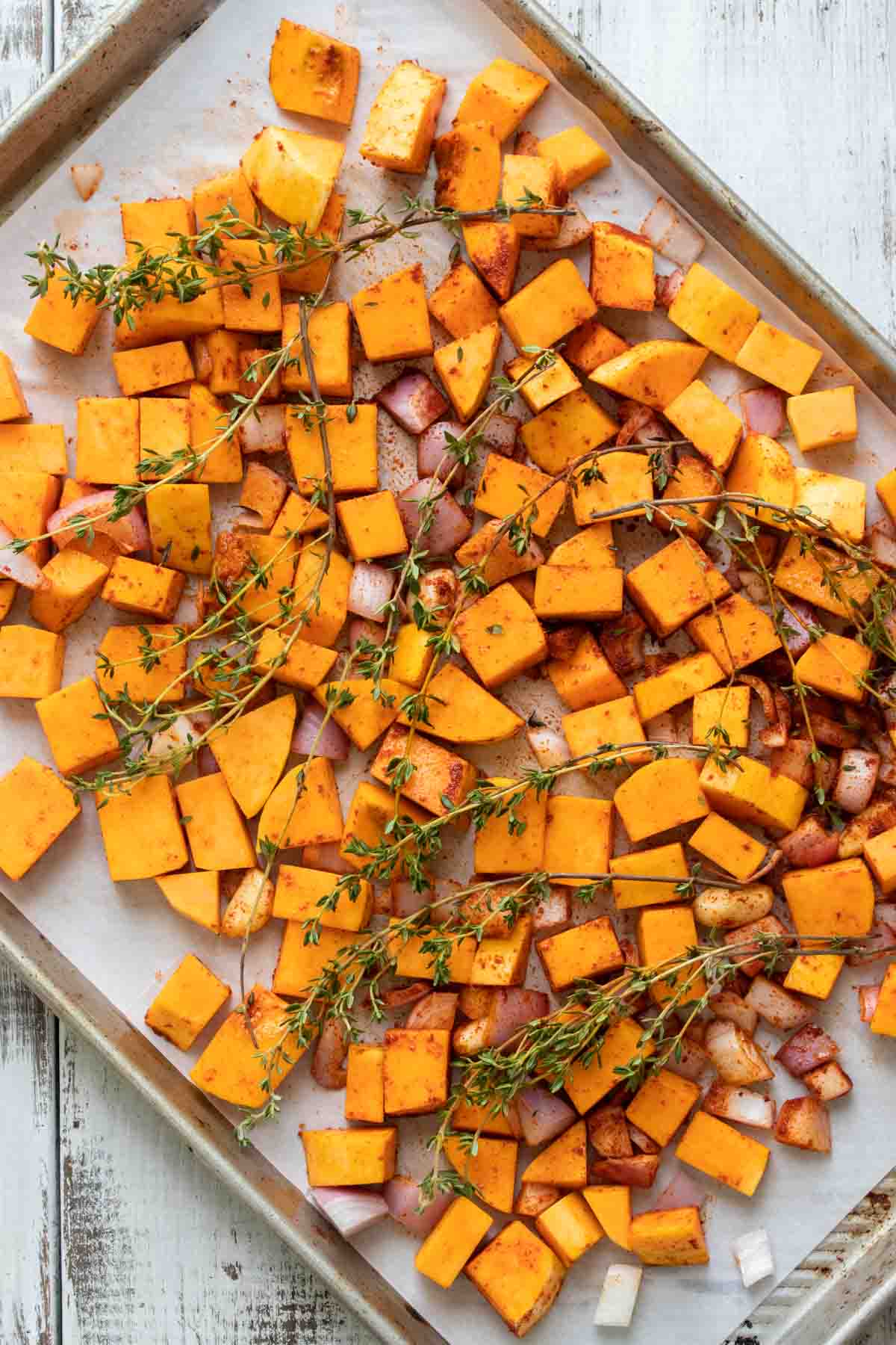 Chopped butternut squash and shallots with sprigs of thyme on a parchment lined baking sheet.
