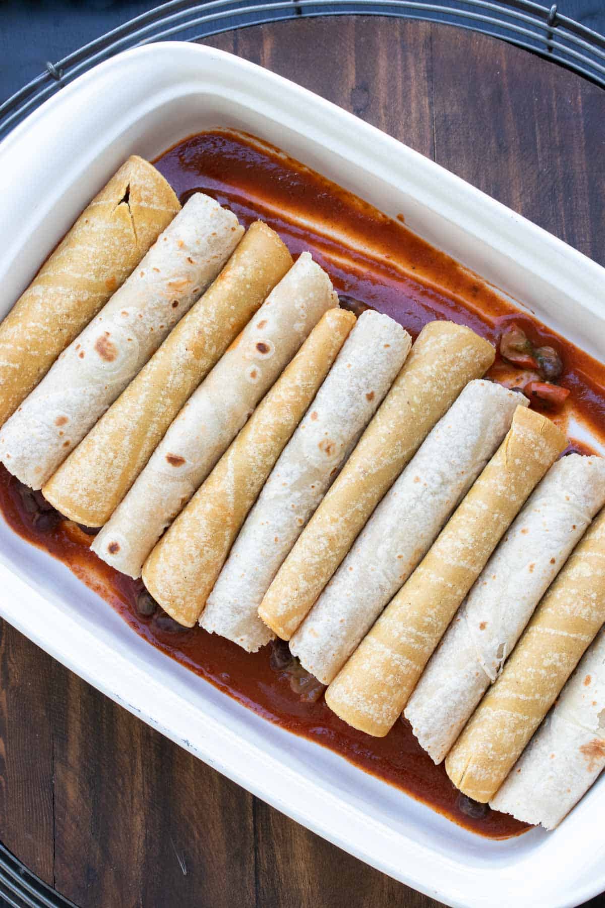 A white baking dish with enchilada sauce and folded enchiladas in it.