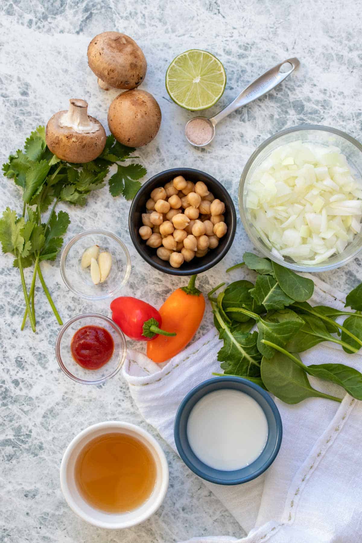 Top view of a group of ingredients needed to make a veggie based coconut curry soup with chickpeas on a grey surface.