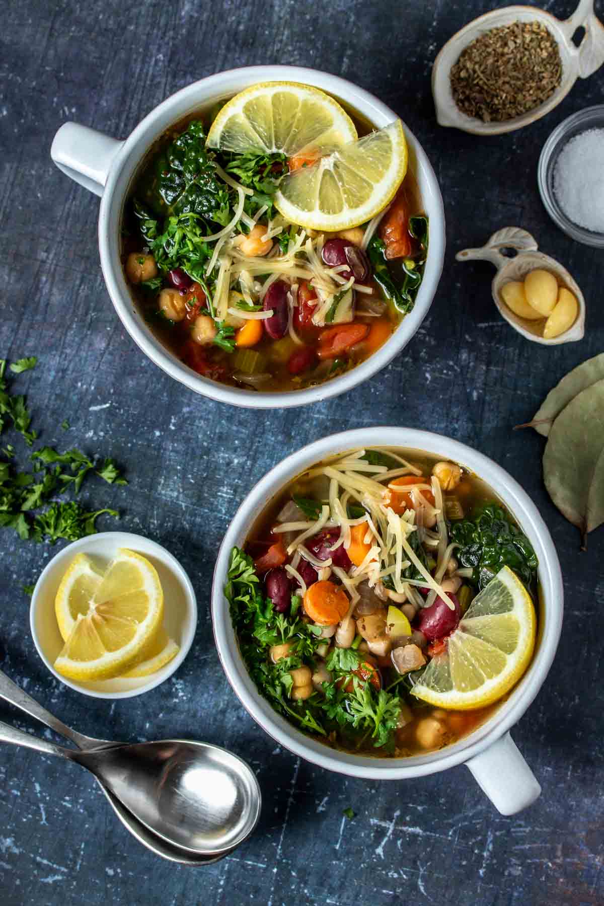 Top view of two soup bowls filled with a vegetable bean soup and topped with lemon, parmesan and parsley.