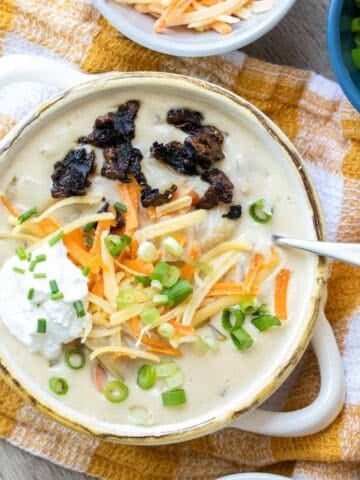 Cream bowl with creamy soup inside topped with sour cream, cheese, scallions and bacon.