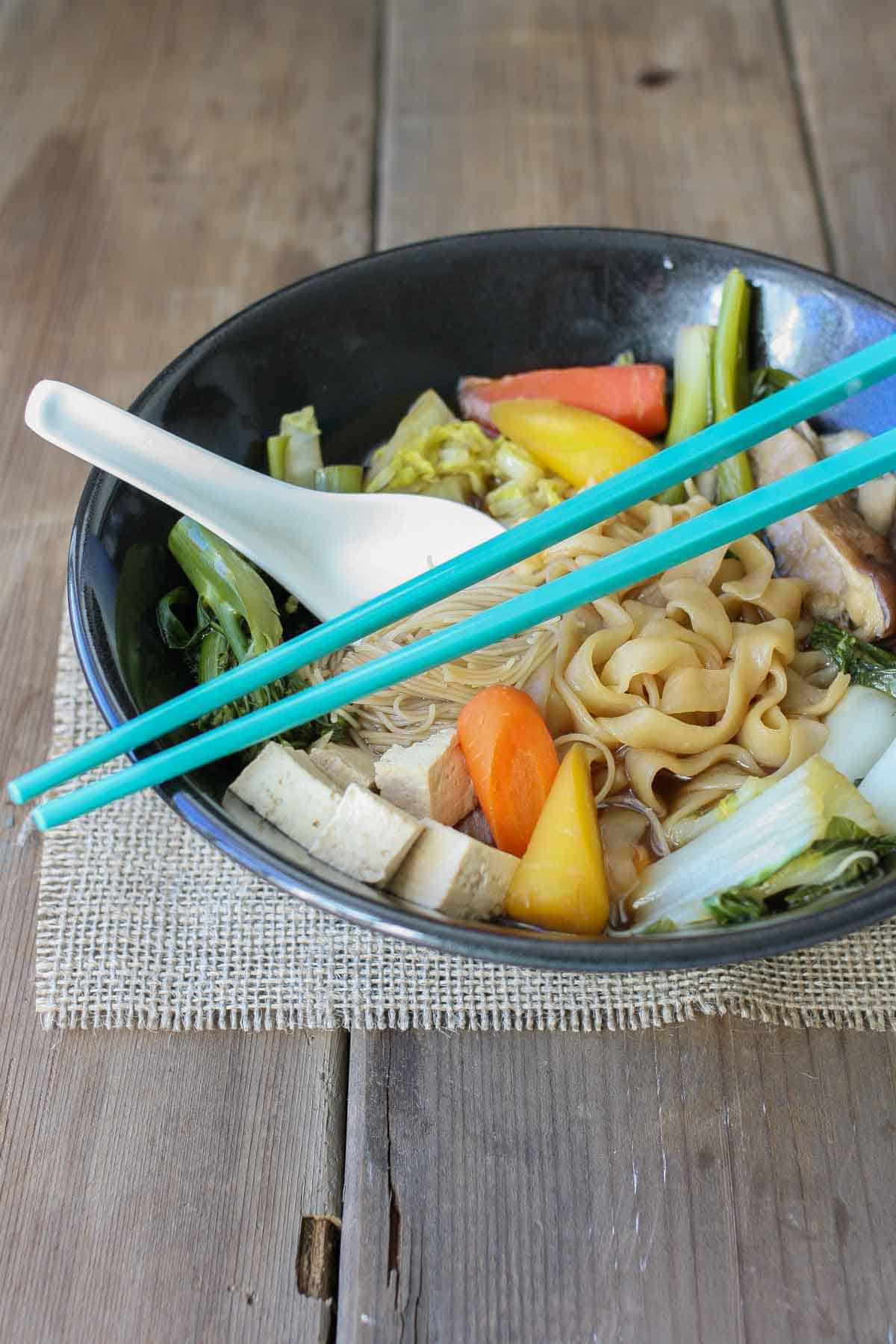 A black bowl with noodles and veggies inside in a broth.