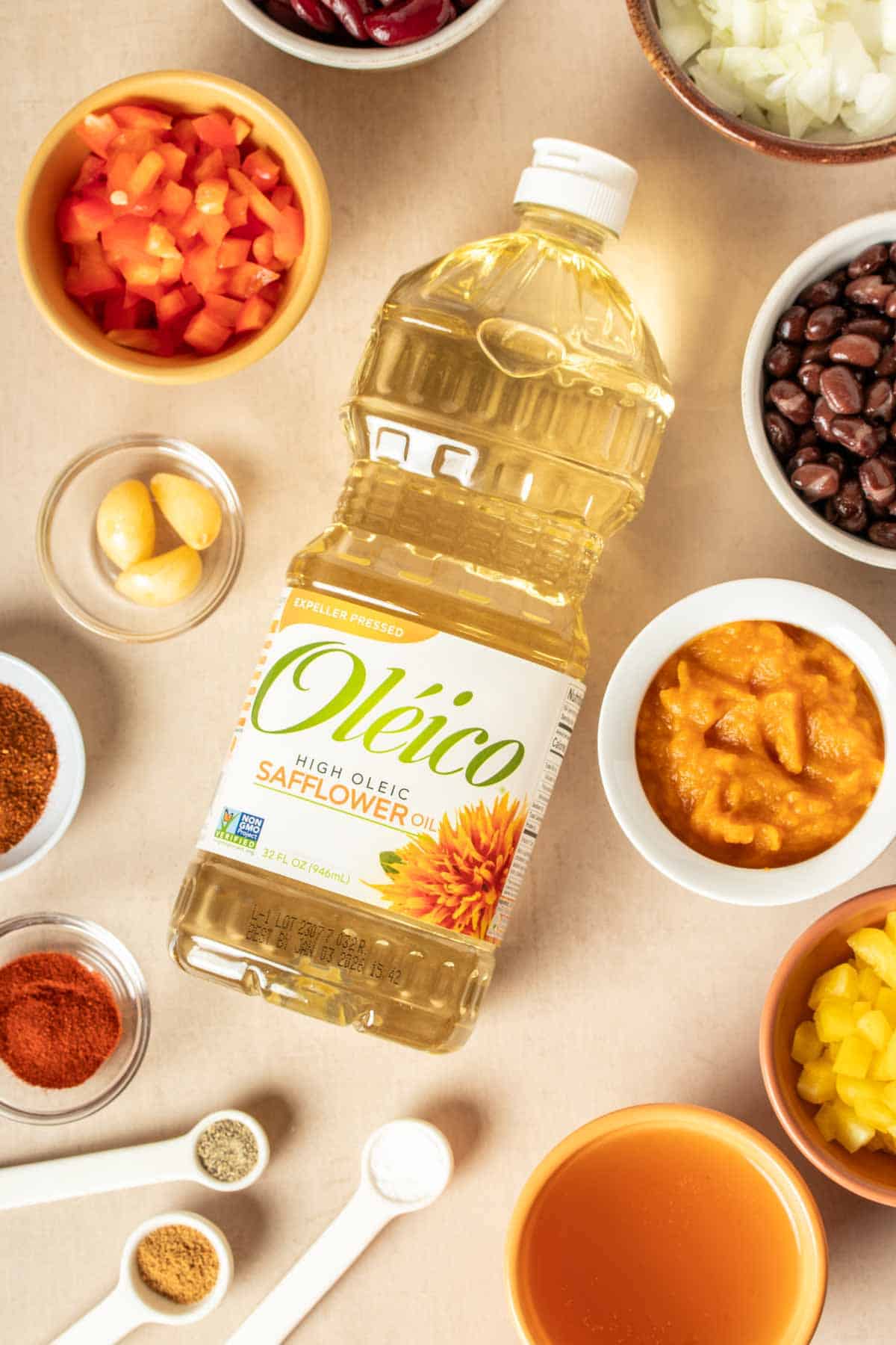 Top view of a bottle of oil laying down surrounded by ingredients needed to make chili.