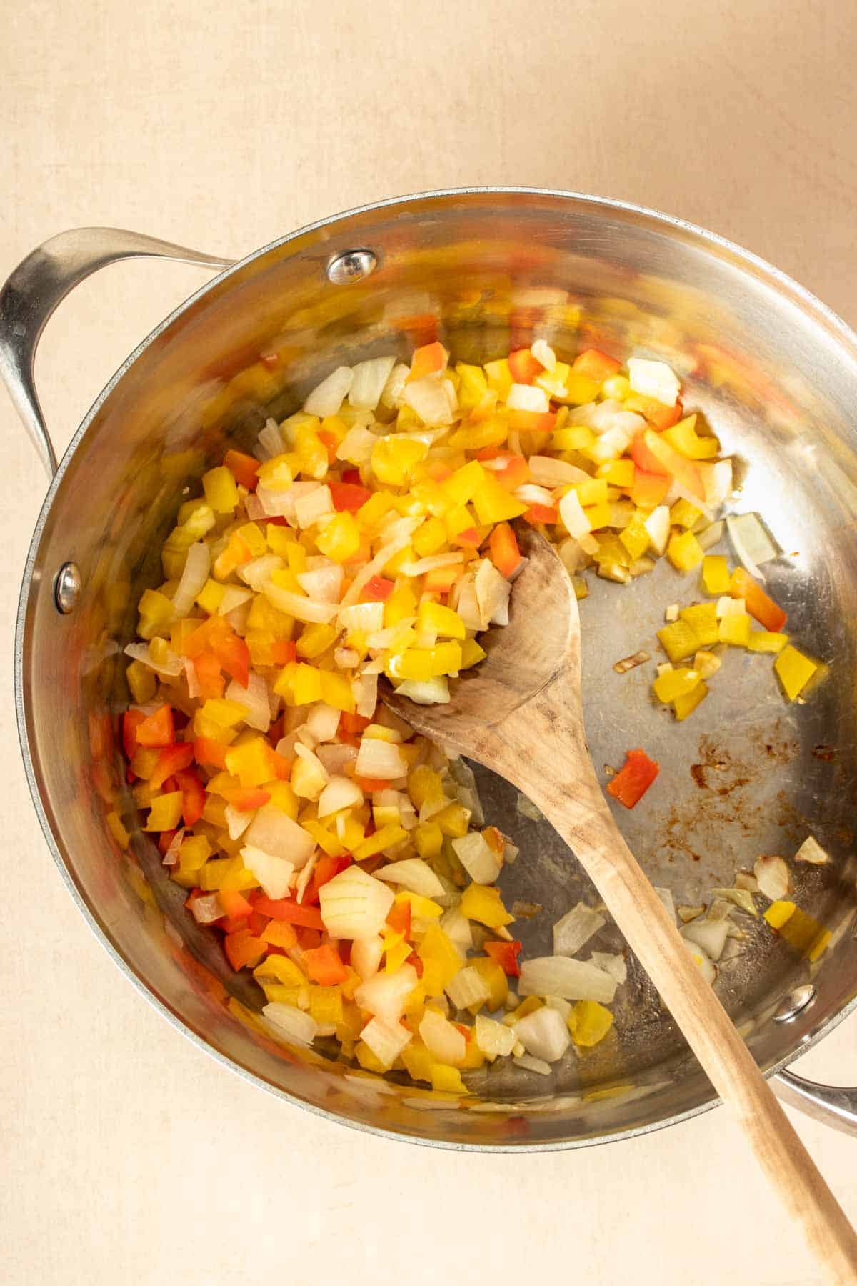 Top view of a metal pot with chopped peppers and onion suateeing inside.