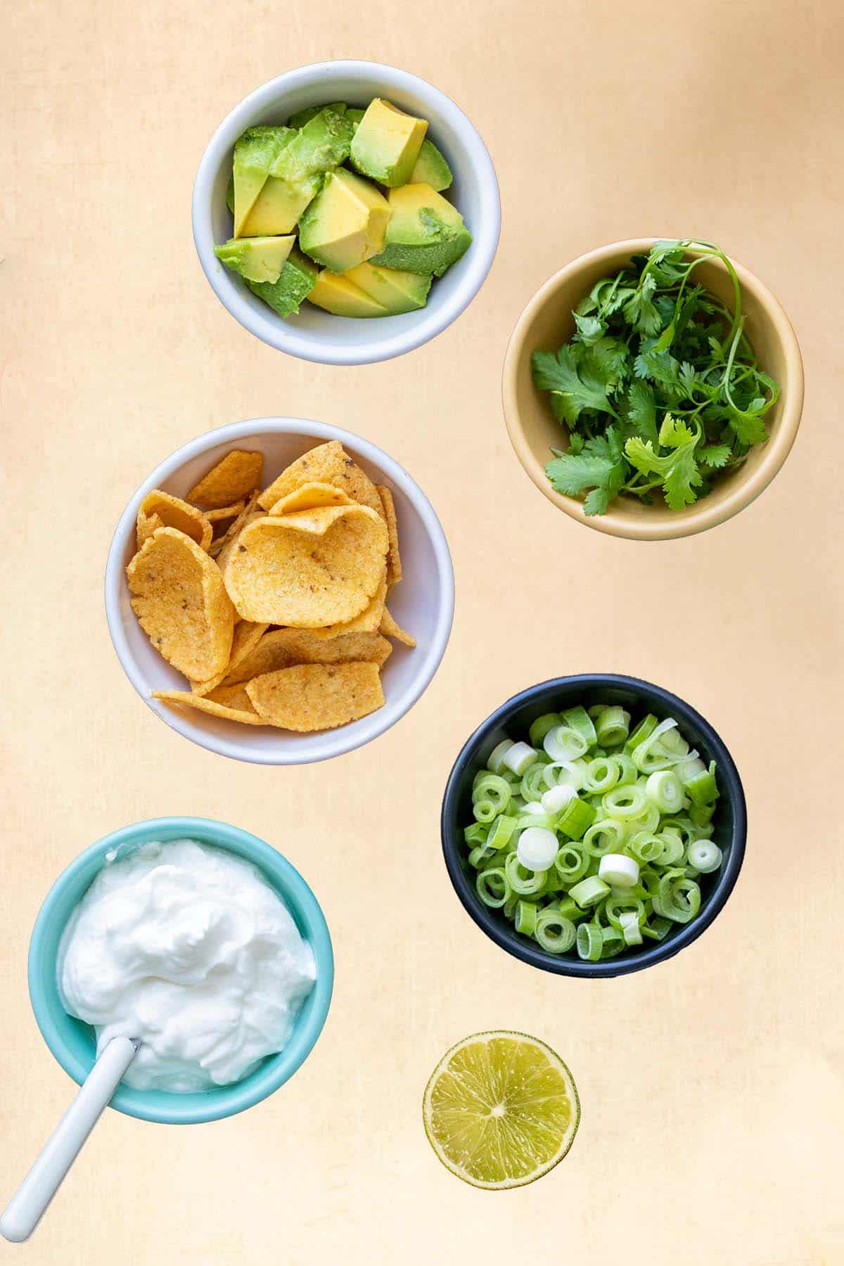 Bowls with toppings that would be used for chili sitting on a tan surface.