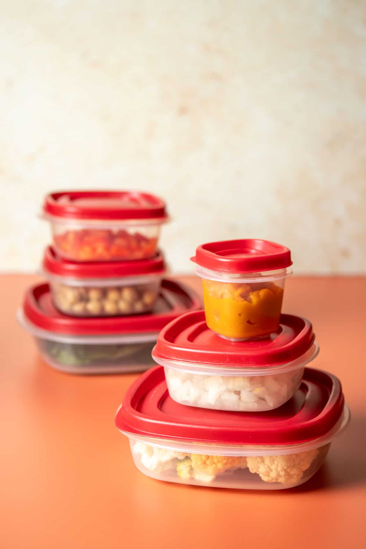 Plastic square containers with red lids stacked up three high on an orange surface with a tan background.