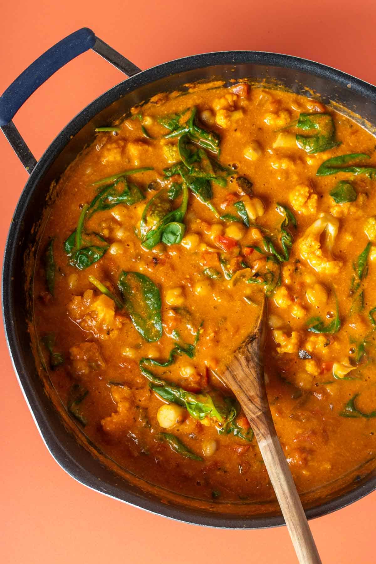 A pan with curry that has chickpeas, cauliflower and spinach in it on an orange surface.