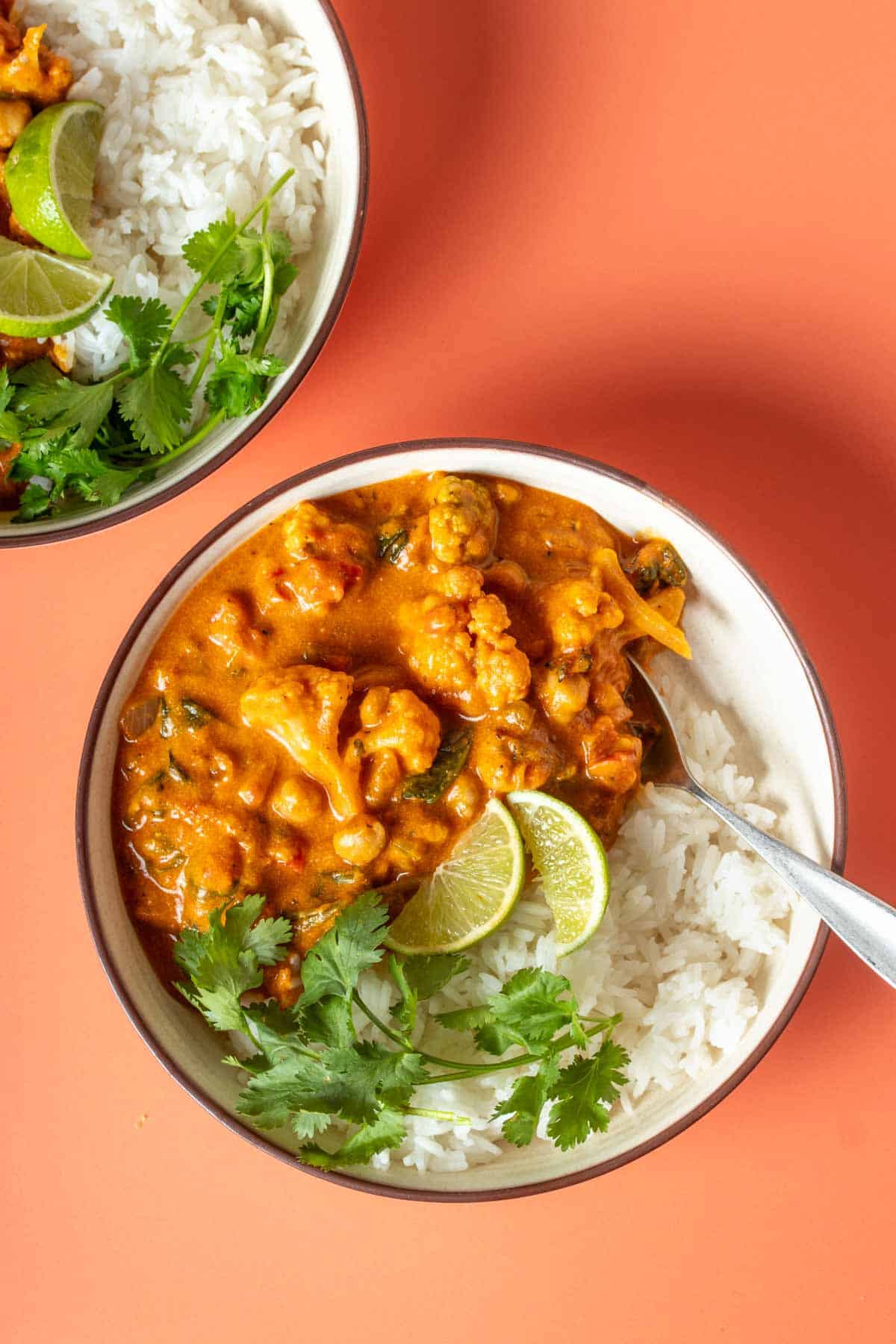 Curry over white rice in a cream bowl topped with cilantro and lime slices.