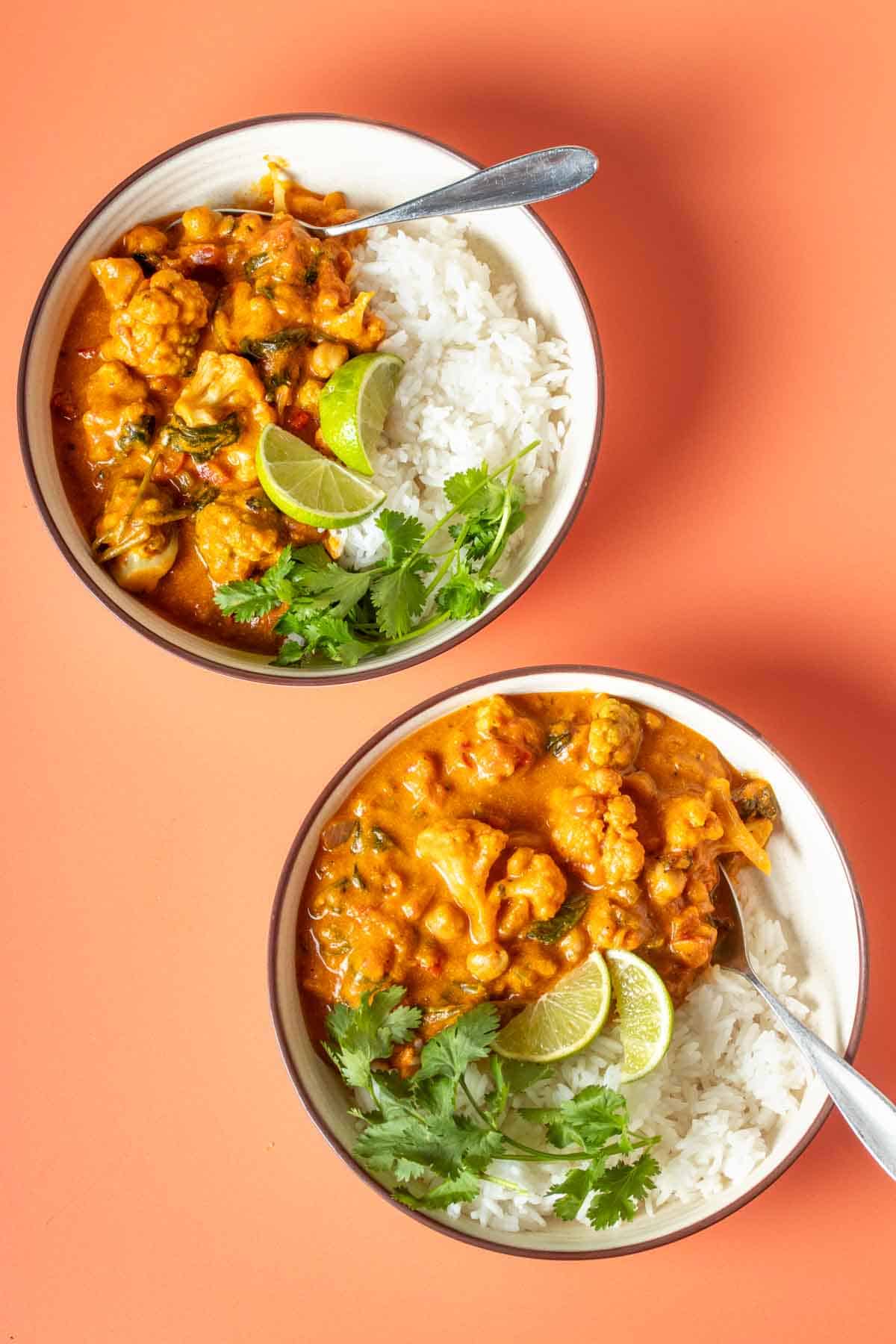 An orange surface with two white bowls filled with white rice and topped with curry and forks in the bowls.