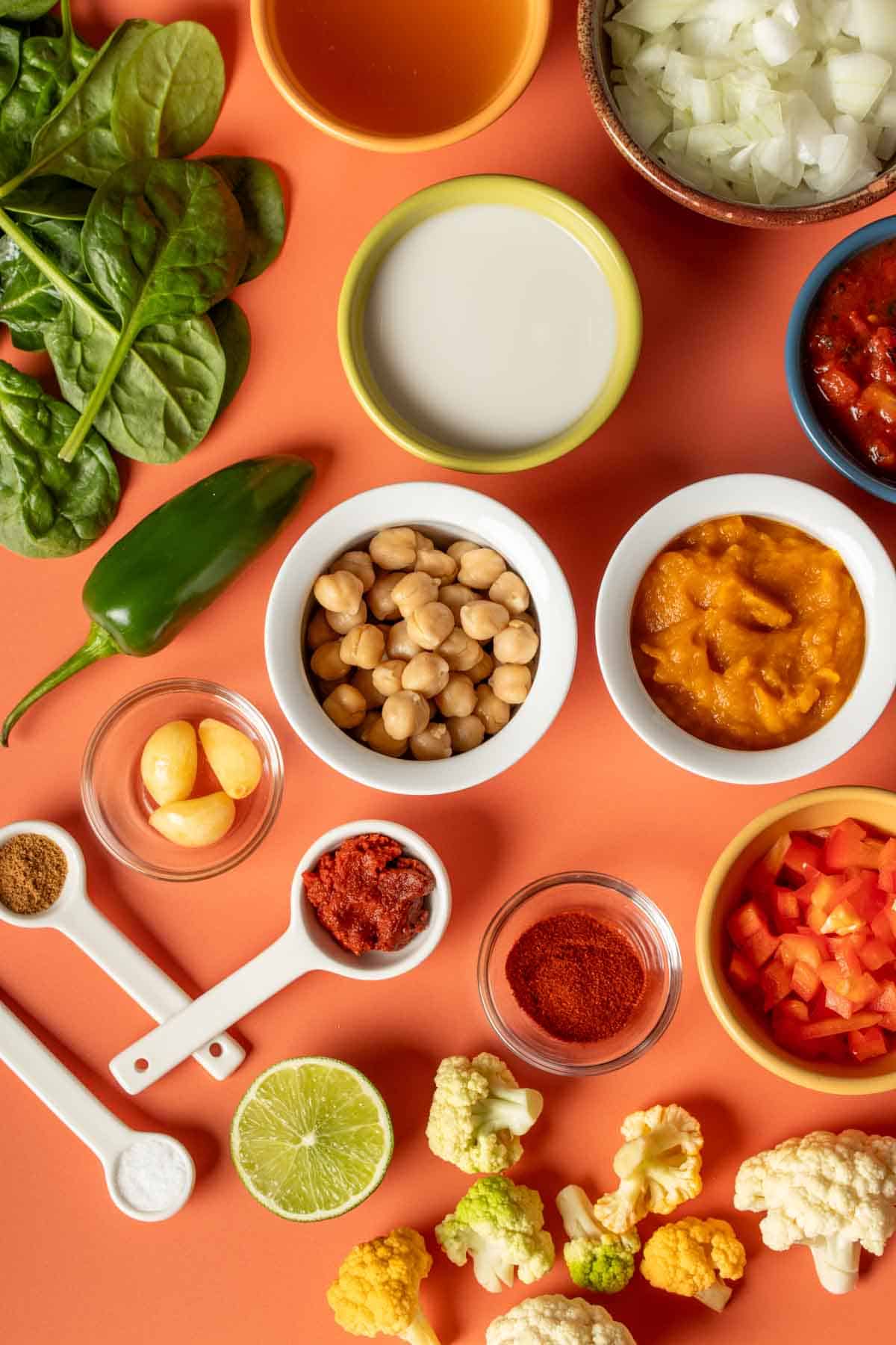 Different bowls and measuring spoons with the ingredients needed to make a pumpkin curry with chickpeas and cauliflower.