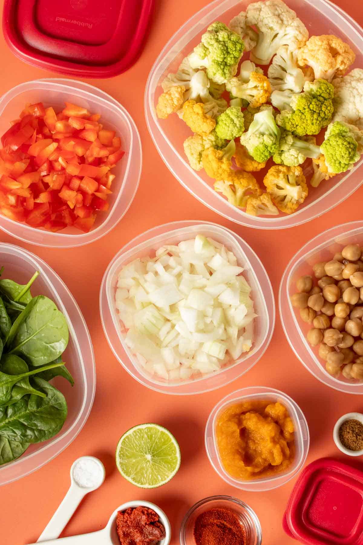 Top view of plastic square containers filled with ingredients needed to make a chickpea pumpkin curry with cauliflower.