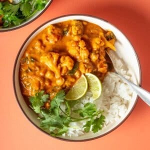 White rice topped with curry and cilantro sprigs and lime slices witting on an orange surface.