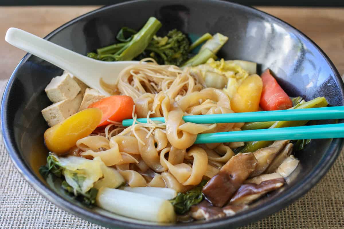 Chopsticks grabbing some noodles from a bowl with veggie sukiyaki in it.