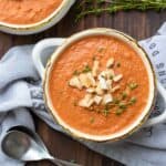 Creamy tomato soup topped with crushed crackers and thyme springs in a white soup bowl.