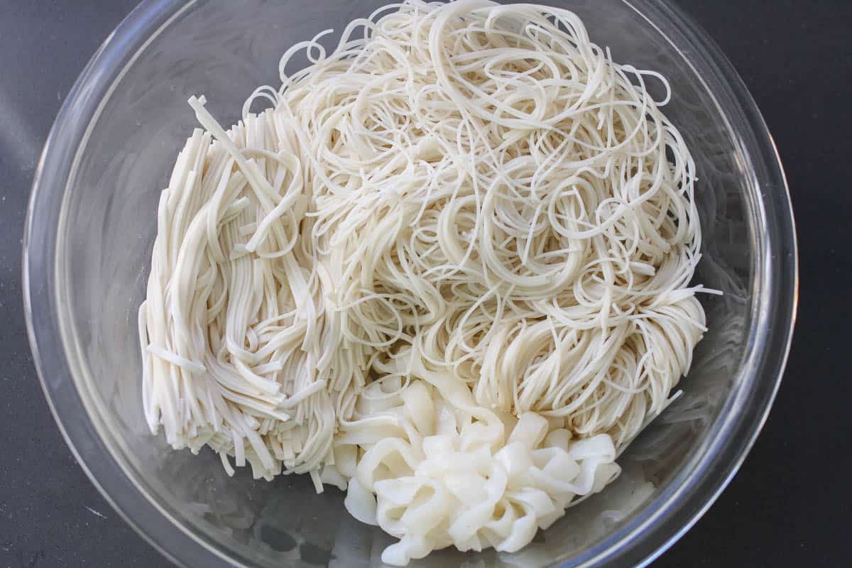 Piles of three different kinds of long noodles in a glass bowl.