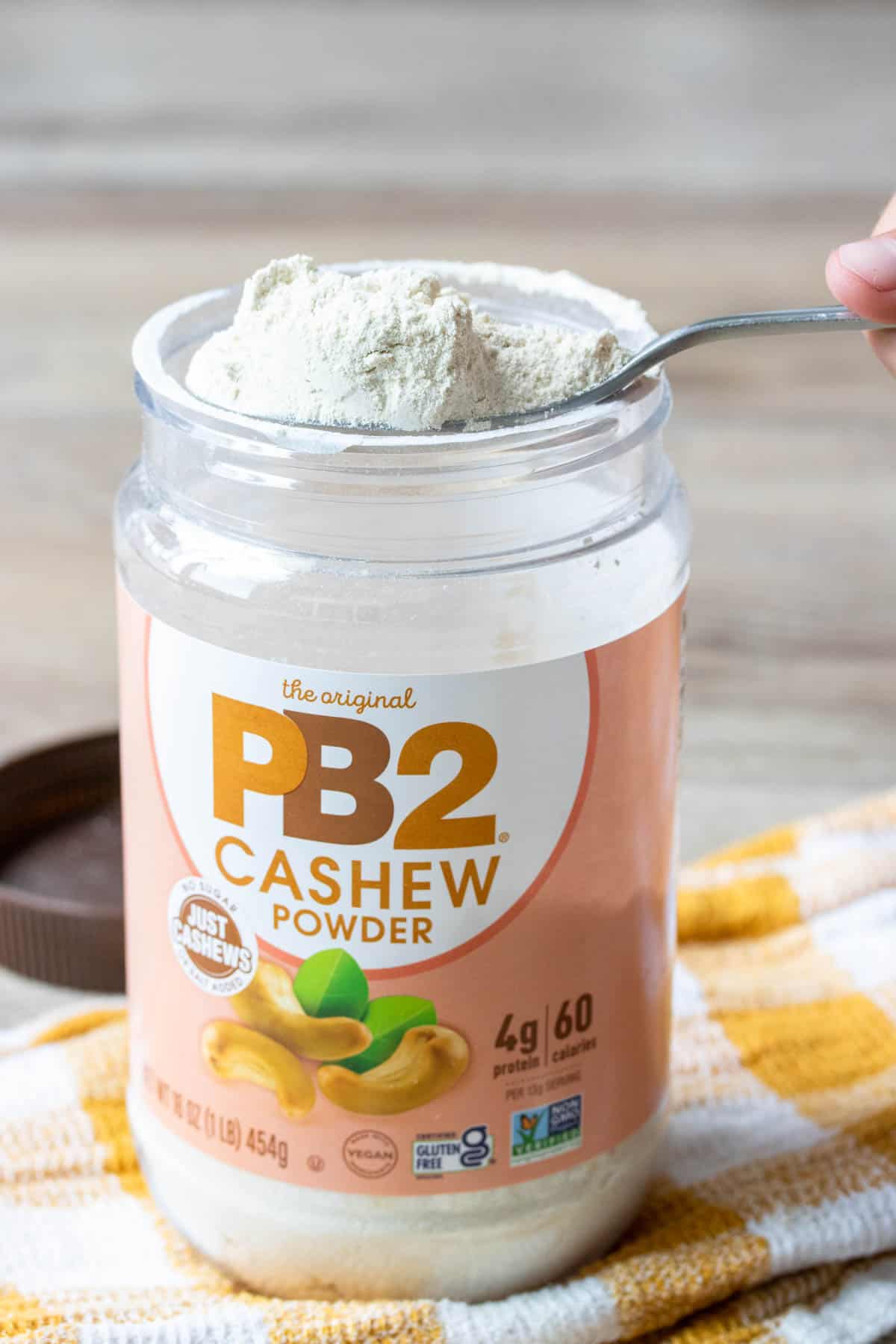 Spoon getting a scoop out of a container of PB2 cashew powder on a yellow towel.