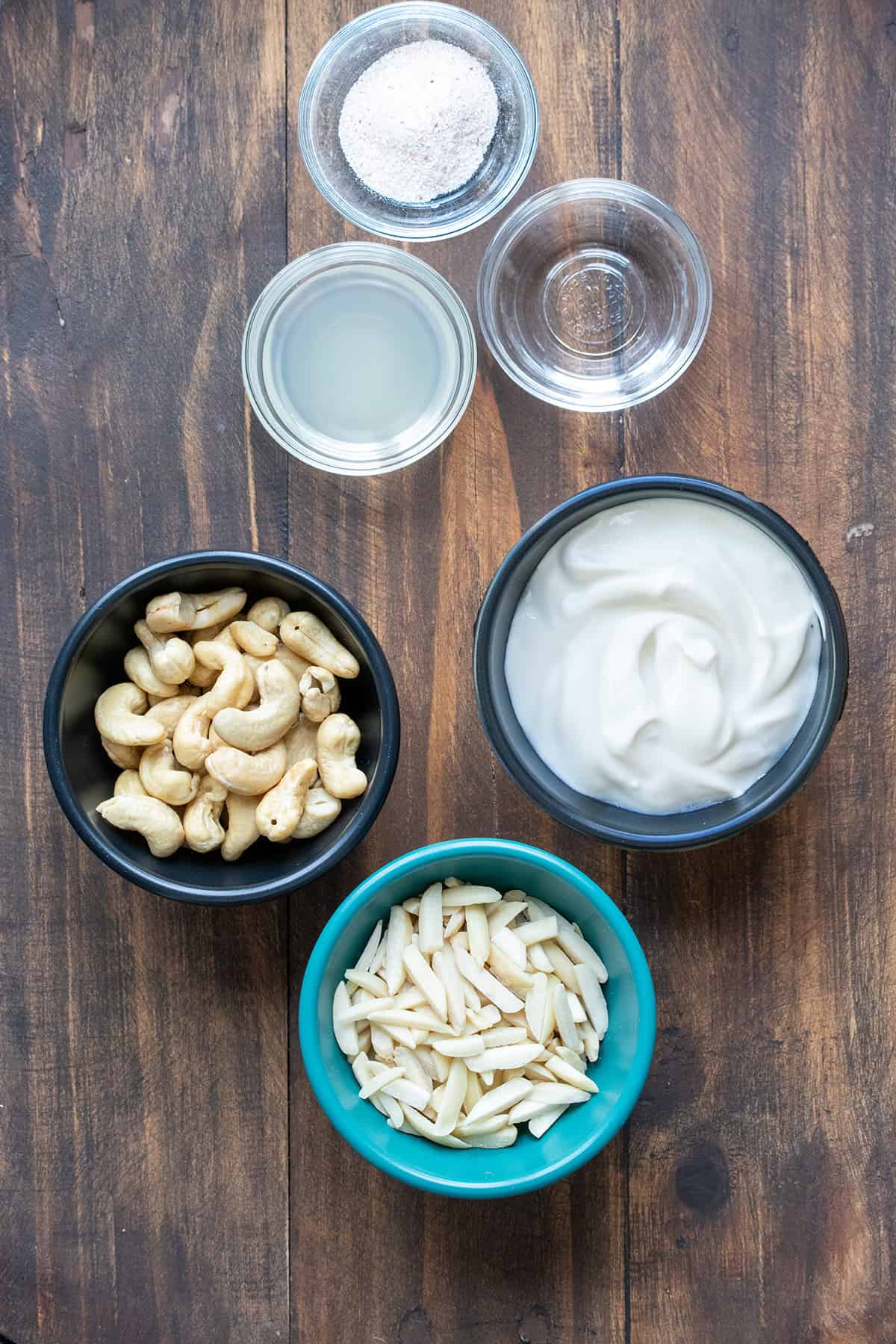 Different colored and sized bowls filled with nuts, yogurt, lemon juice, vinegar and salt.