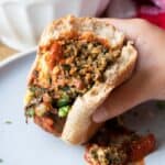 A half eaten meatball sub with marinara and fresh parsley being held over a white plate.