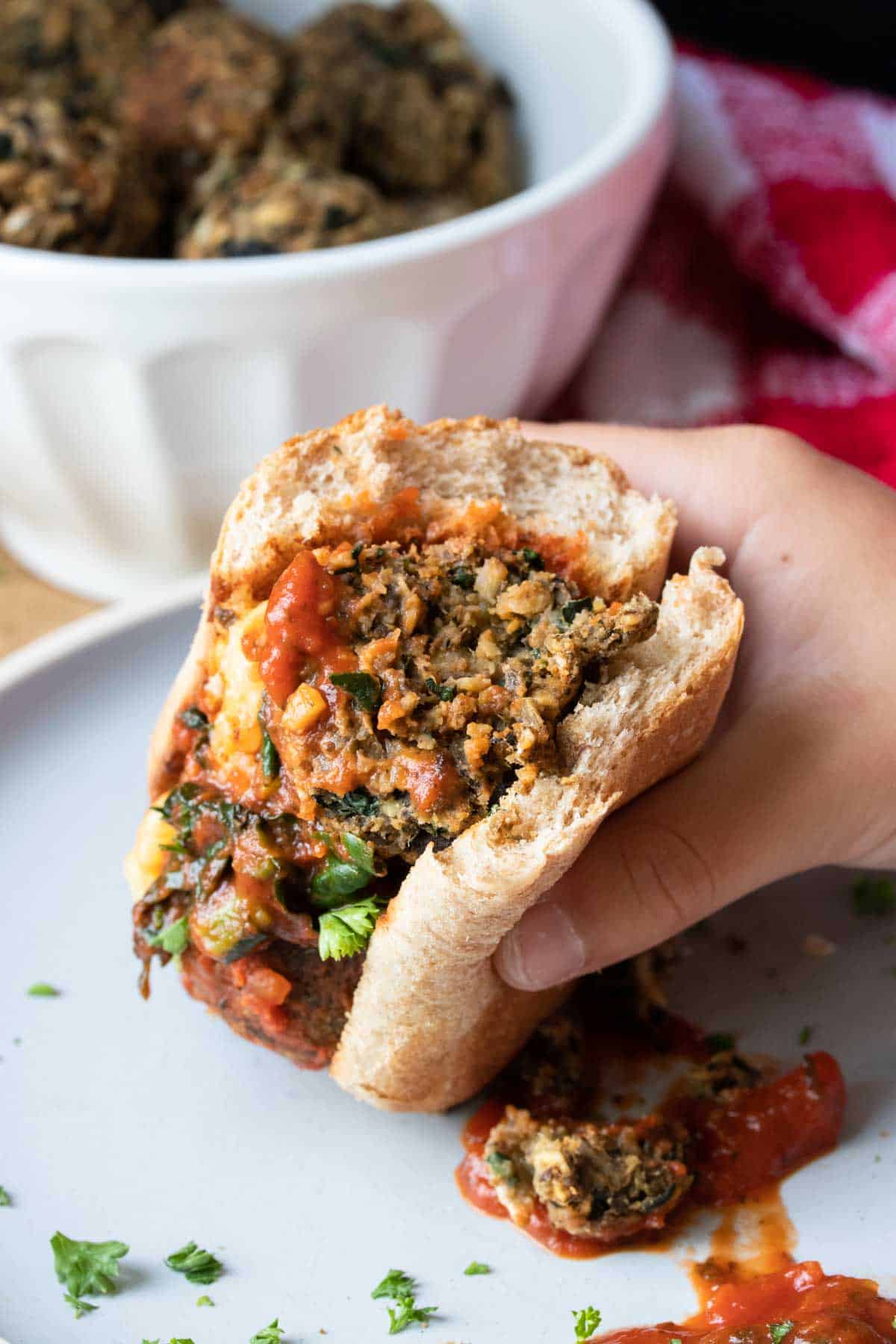 Hand holding a half eaten vegan meatball sub sandwich.