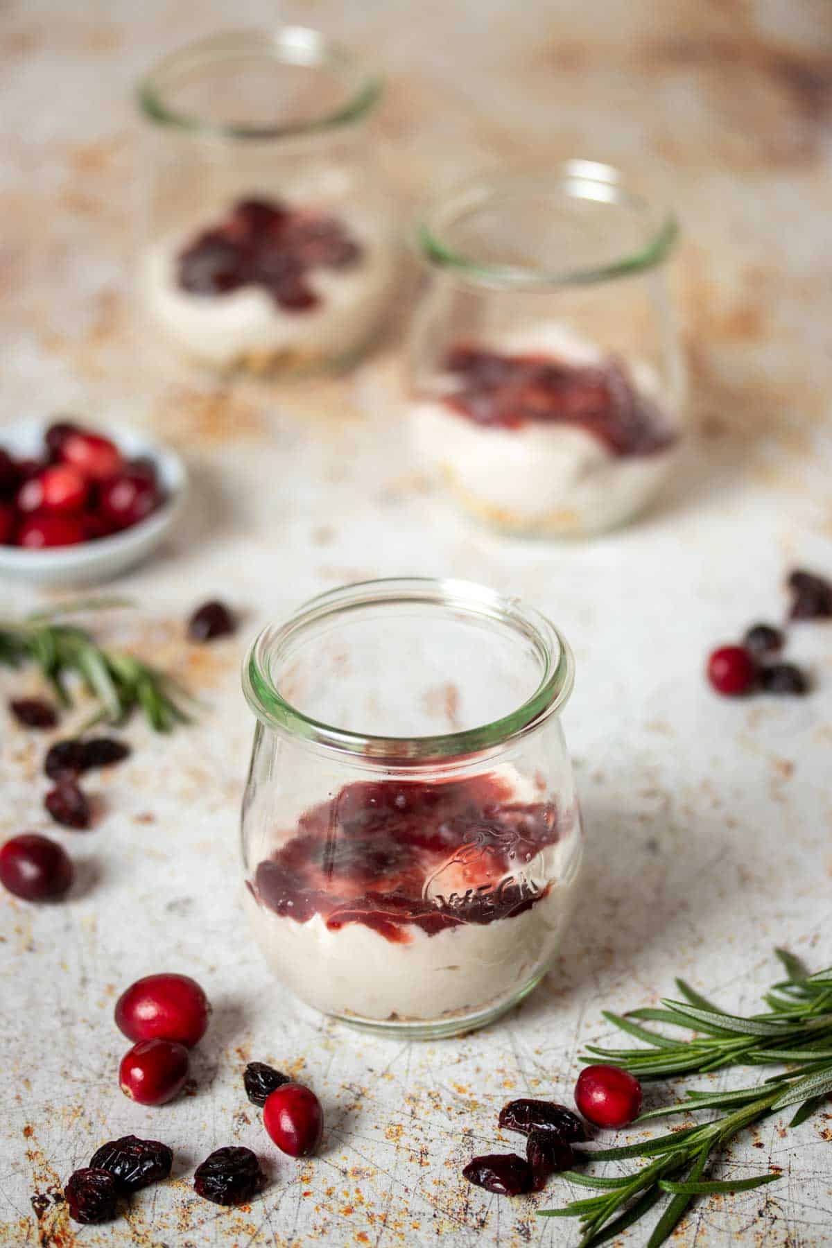 Yogurt and jelly layered in a glass jar and two other jars behind it all sitting on a tan speckled surface.