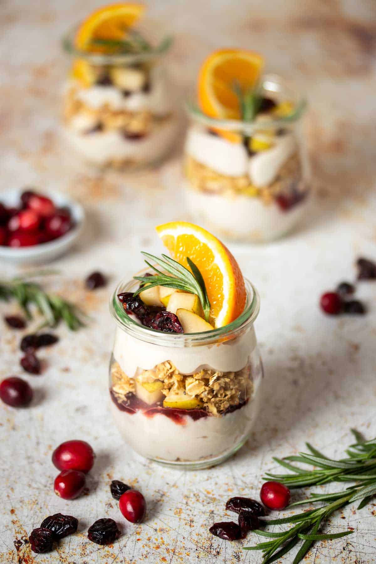 Three glass jars of breakfast parfaits with yogurt, fruit and granola in front of each other.