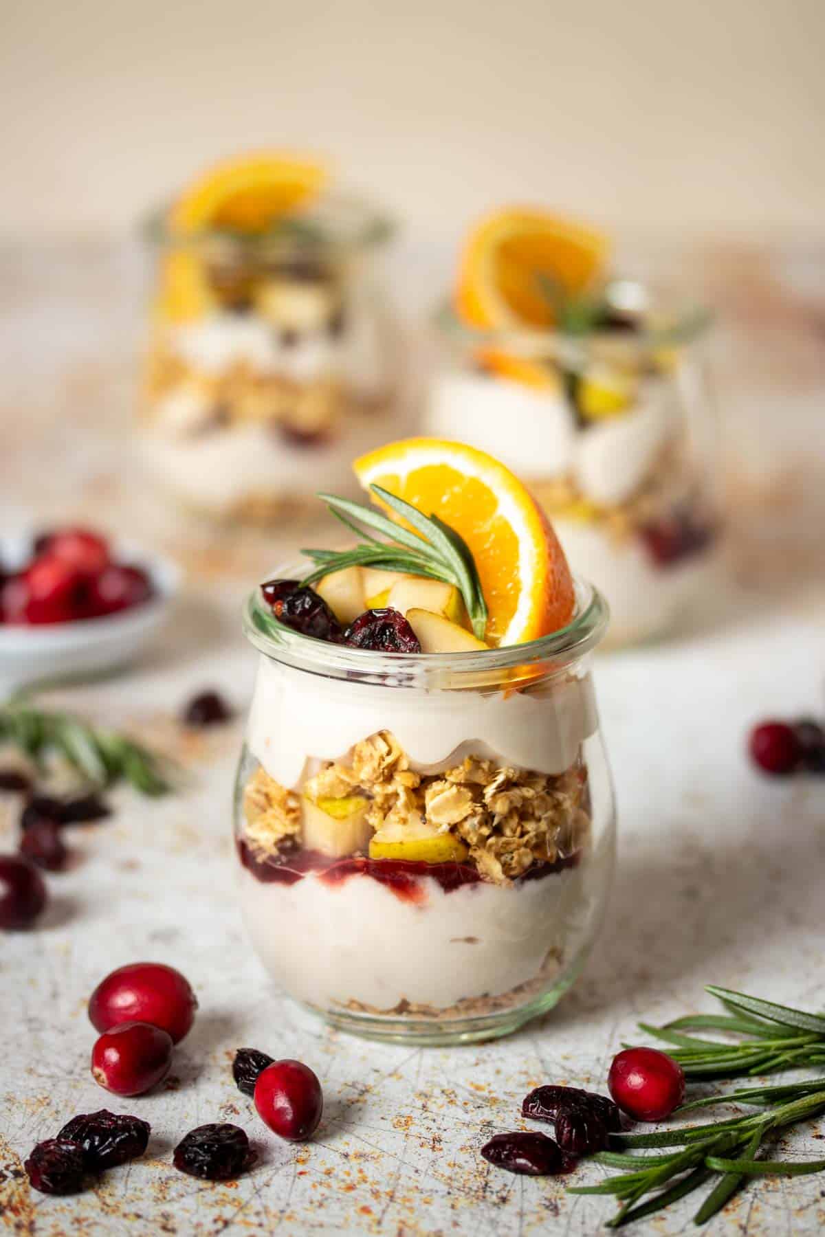 A layered breakfast parfait with yogurt, granola and fruit in a glass jar topped with an orange slice.