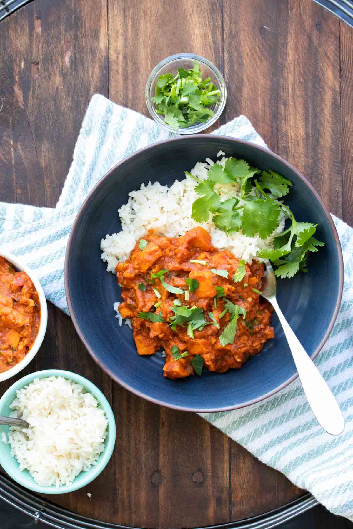 Black plate with sweet potato red curry over white rice with a cilantro sprig.