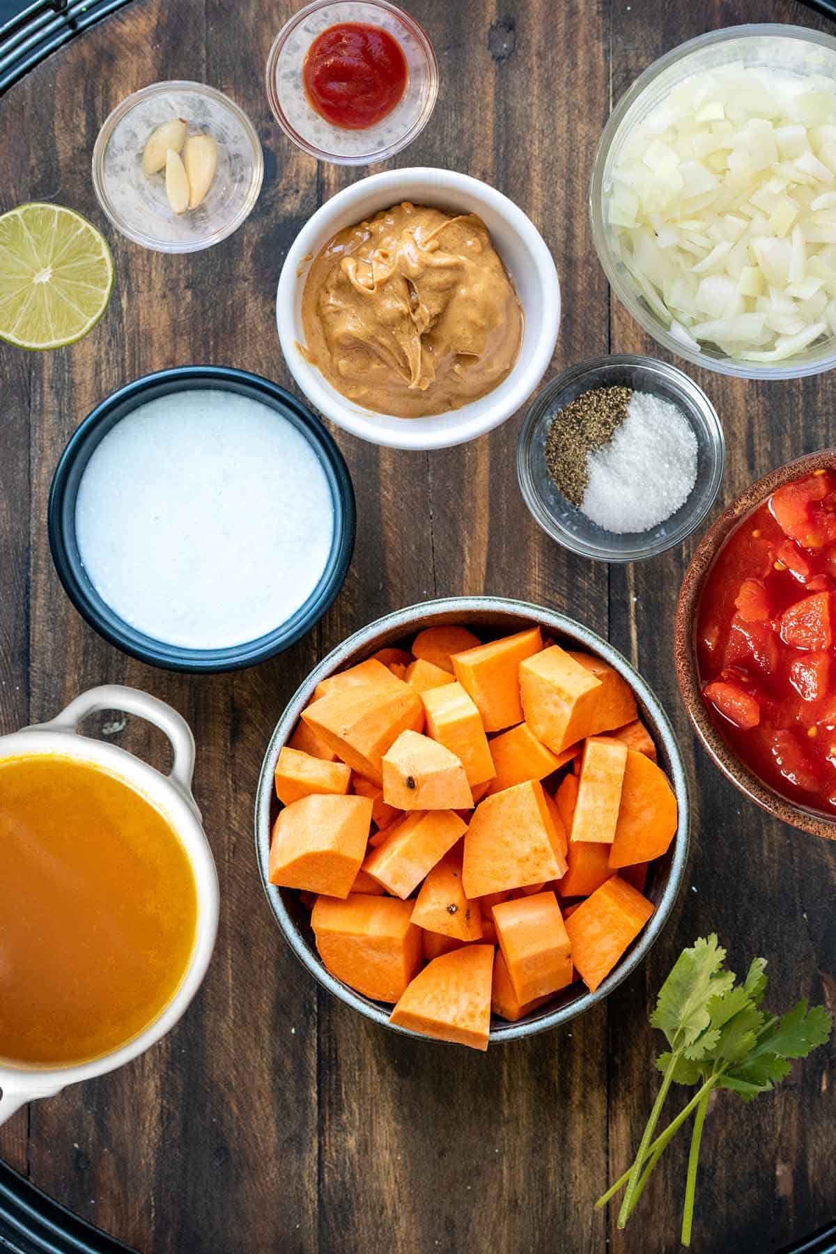 A wooden surface with different bowls filled with ingredients to make a red sweet potato curry.