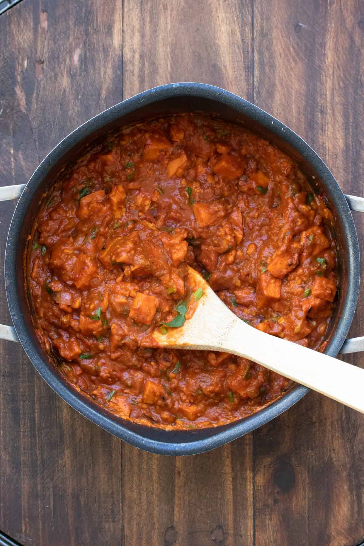 Cooked sweet potato red curry being stirred in a pot.