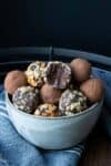 A grey bowl on a darker grey towel filled with truffles topped with different things.