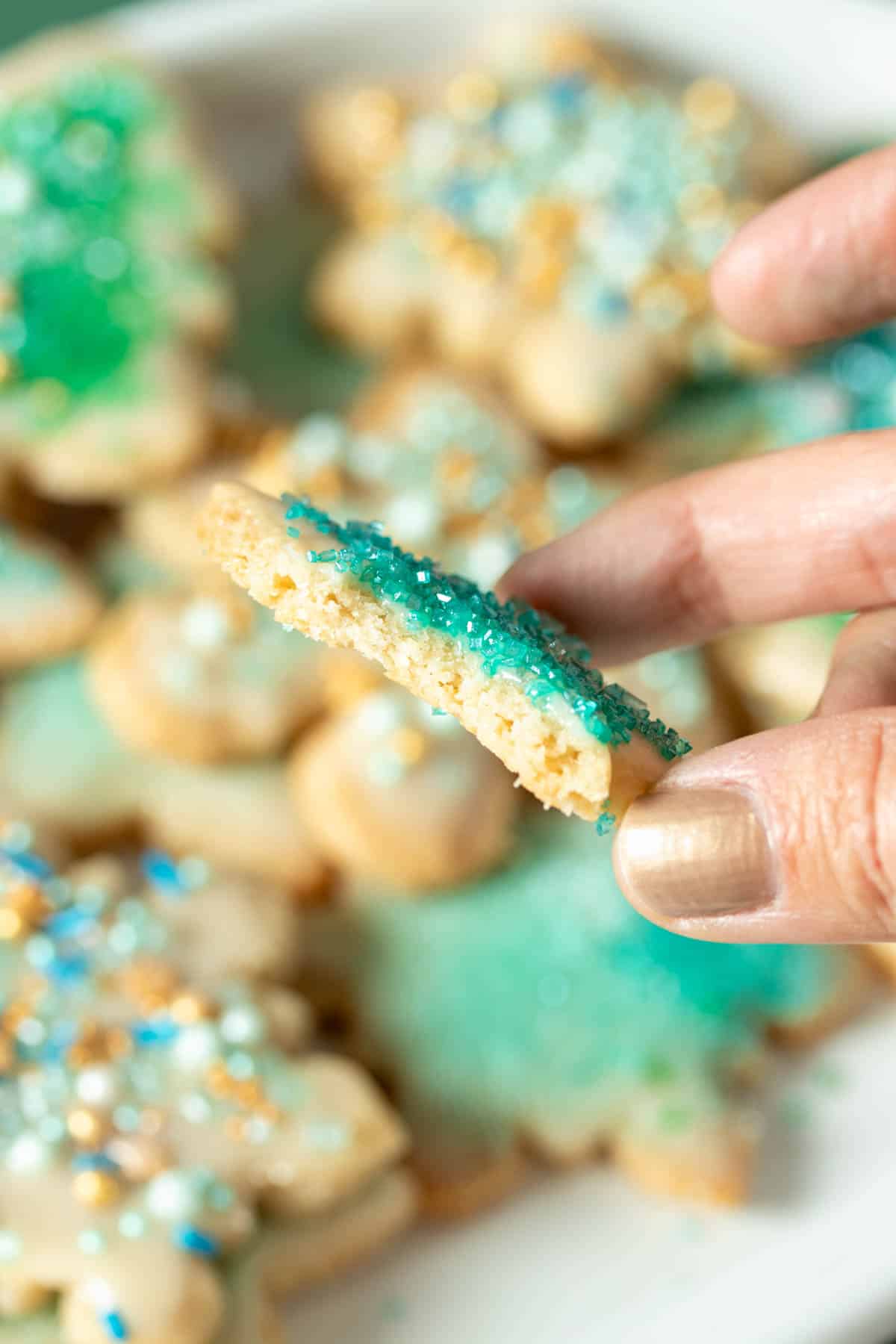 A hand holding a sugar cookie with a bite out of it sideways so you can see the inside.