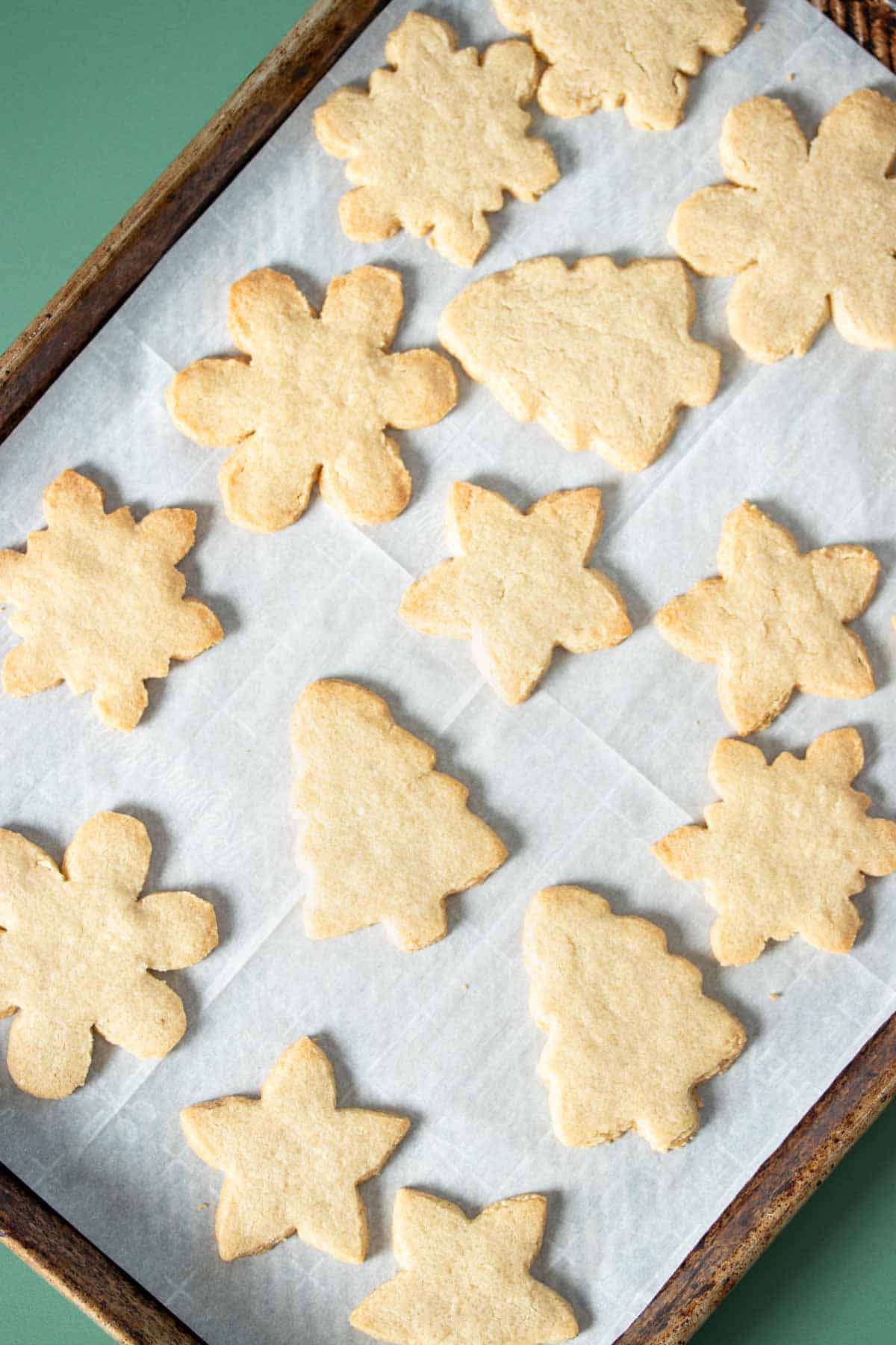 Baked sugar cookies in holiday shapes on a parchment lined baking sheet.