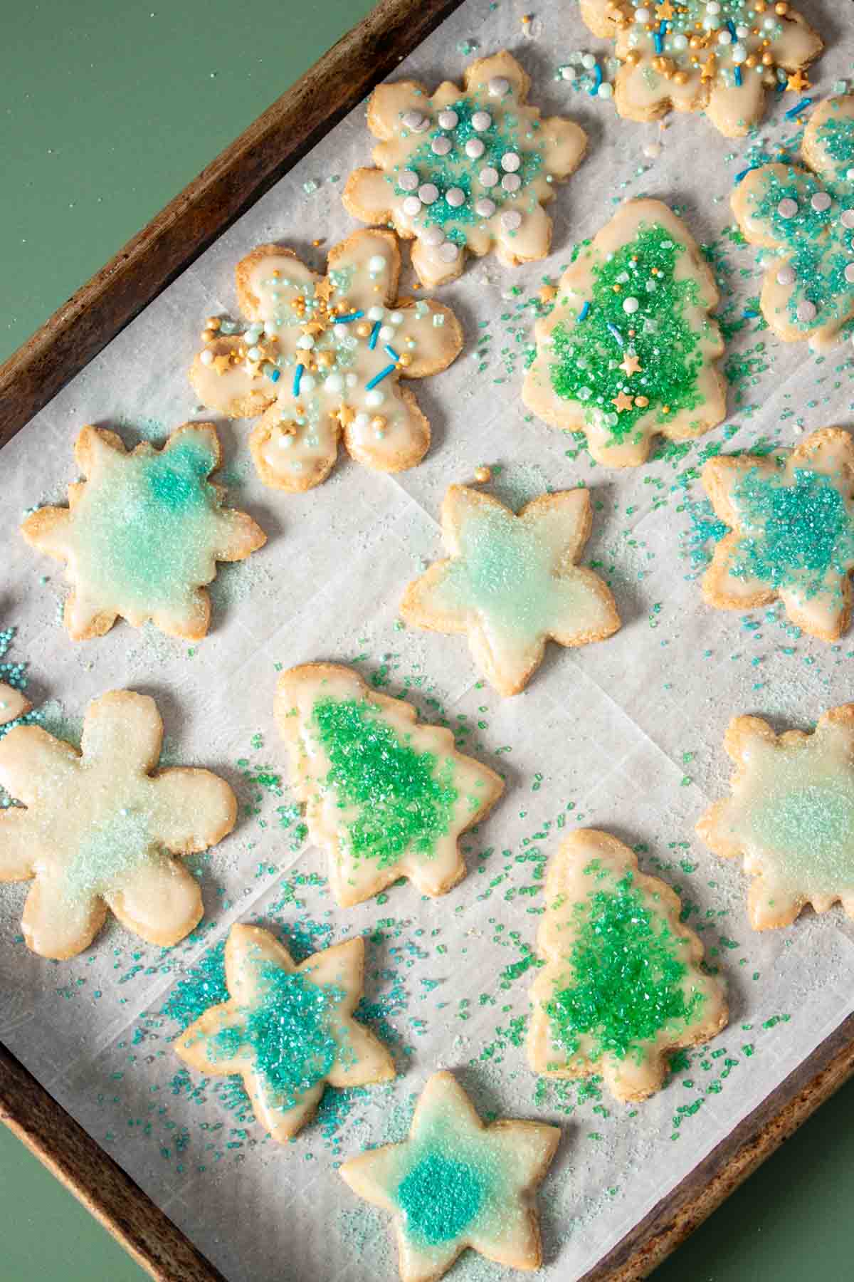 Holiday shaped sugar cookies decorated with green and blue decor on a parchment lined baking sheet.