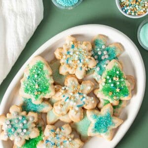 A white plate with blue and green decorated sugar cookies piled on top.