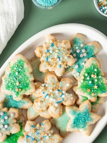 A white plate with blue and green decorated sugar cookies piled on top.