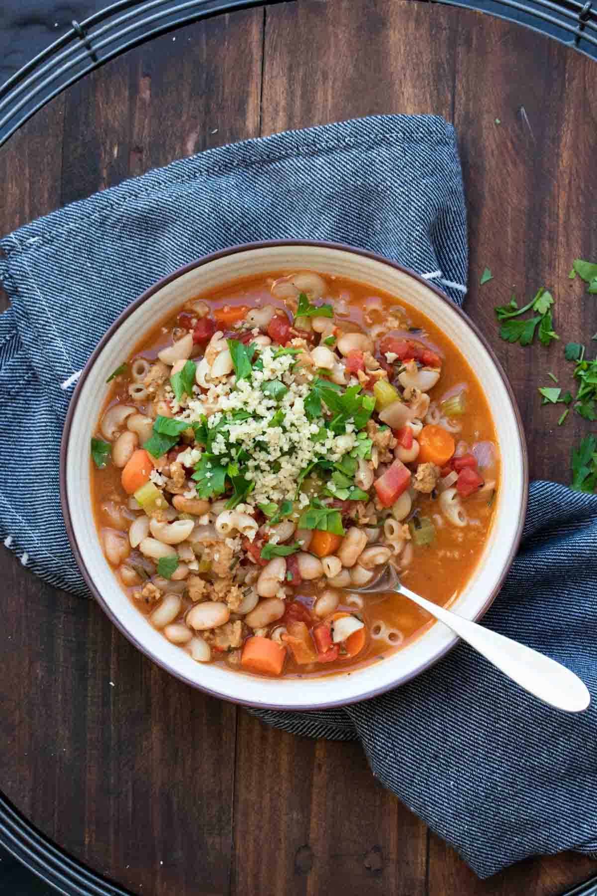 A pasta fagioli soup with beans, vegetables and pasta in a white bowl on a blue towel.