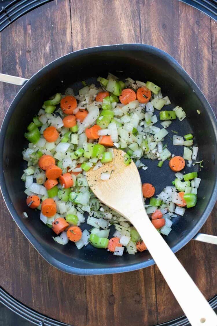 Wooden spoon sautéing vegetables in a pot.